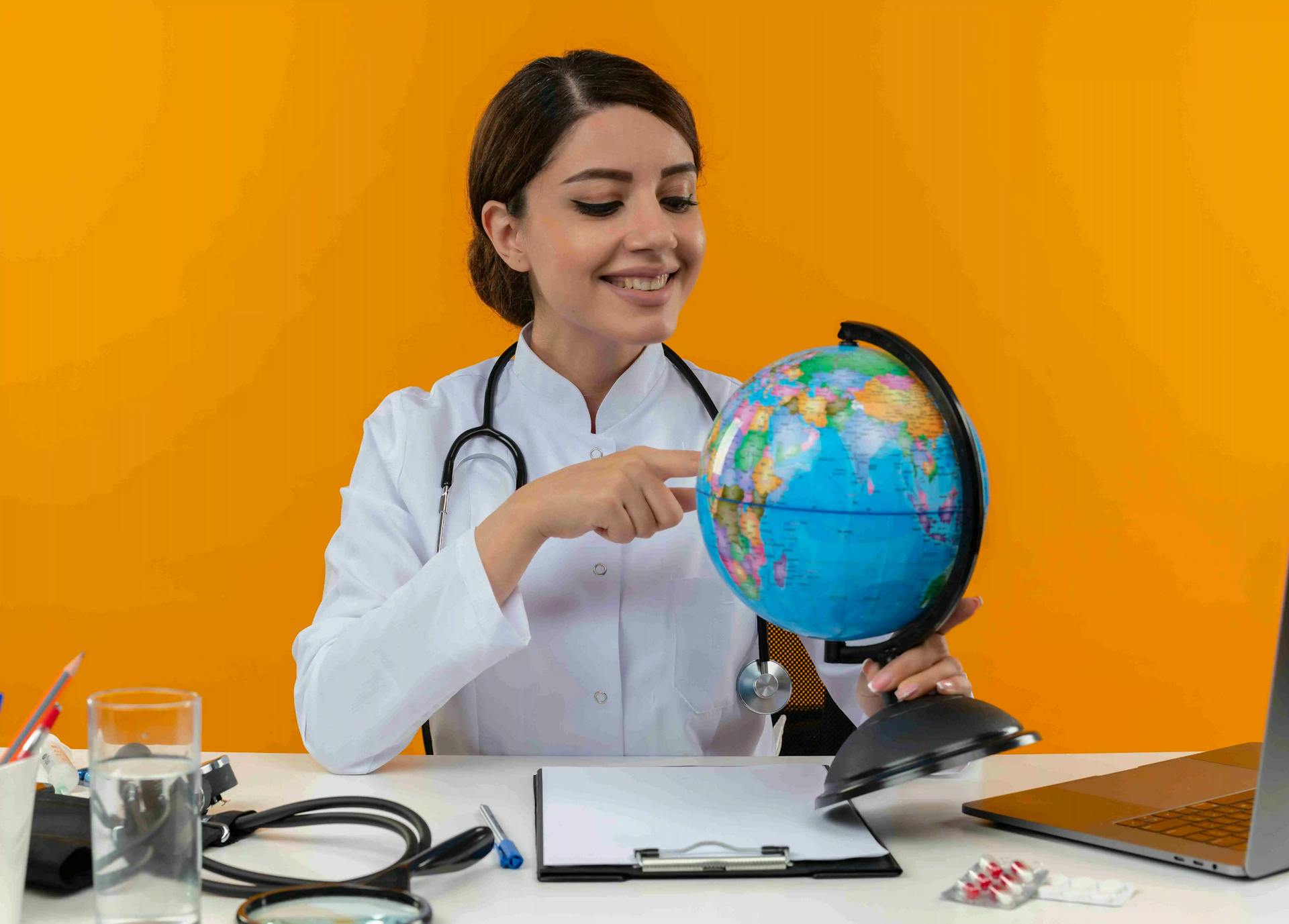 https://strapiassetsprod.s3.amazonaws.com/smiling_young_female_doctor_wearing_medical_robe_stethoscope_sitting_desk_with_medical_tools_laptop_holding_looking_pointing_finger_globe_isolated_yellow_wall_11zon_fcee635d91.webp