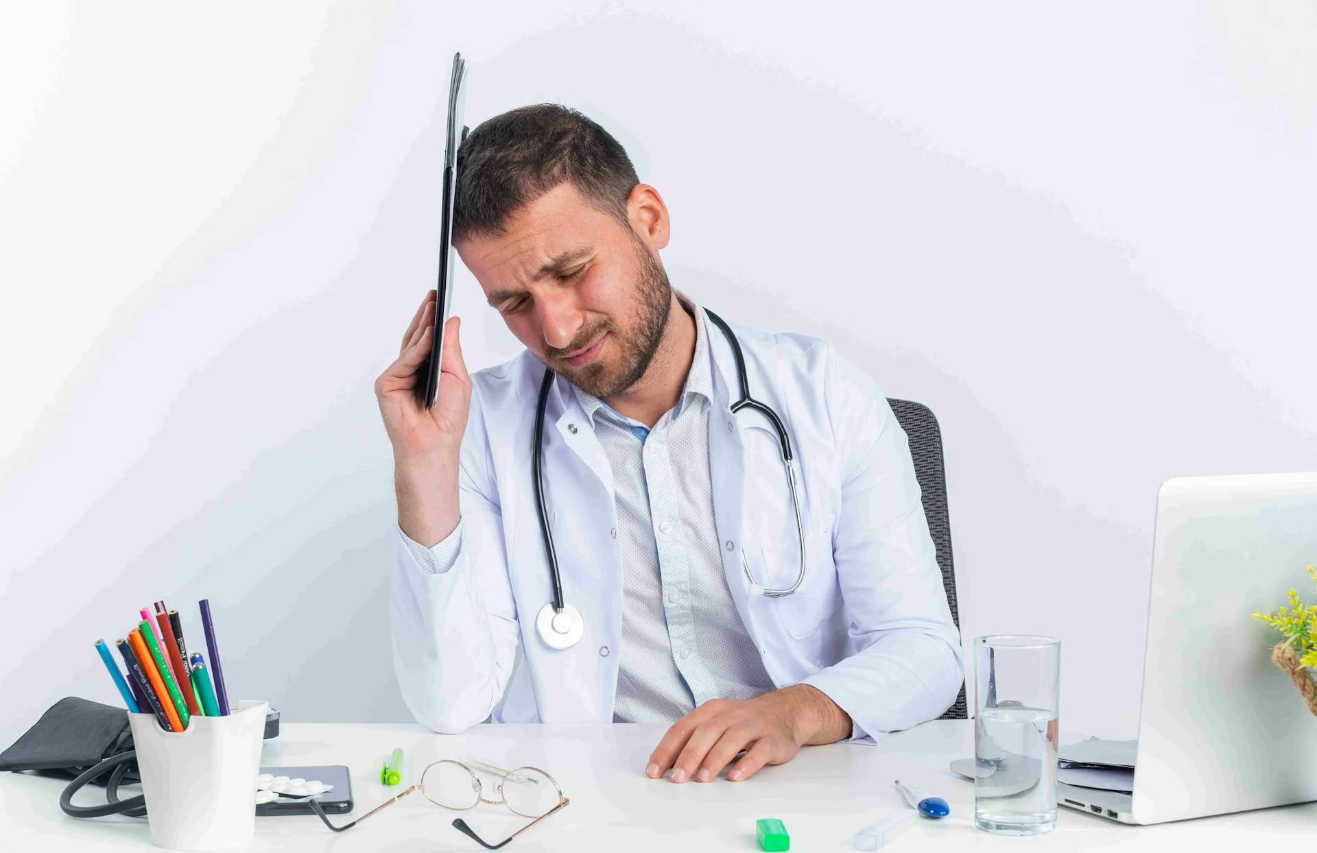https://strapiassetsprod.s3.amazonaws.com/young_man_doctor_white_coat_with_stethoscope_holding_clipboard_his_head_looking_tired_overworked_sitting_table_with_laptop_white_wall_11zon_1_0b505c7751.webp